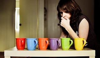 たくさんの色のコップの前に立って、どれを選ぼうか迷っている外国人女性の画像